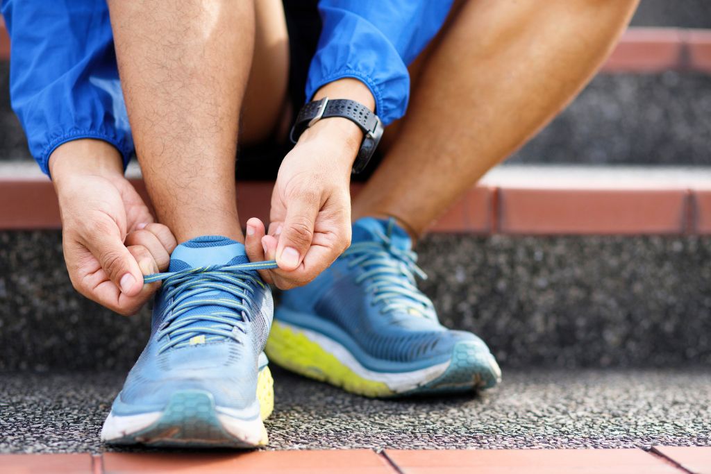 A male athlete sitting on the stairs tying his shoelaces.