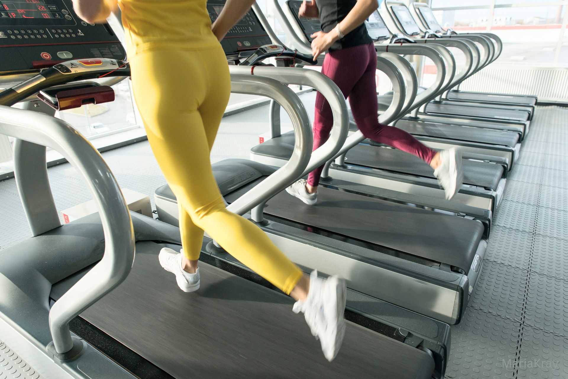Two young women running on the treadmill in the gym. Photo by Maria Kray via Canva.